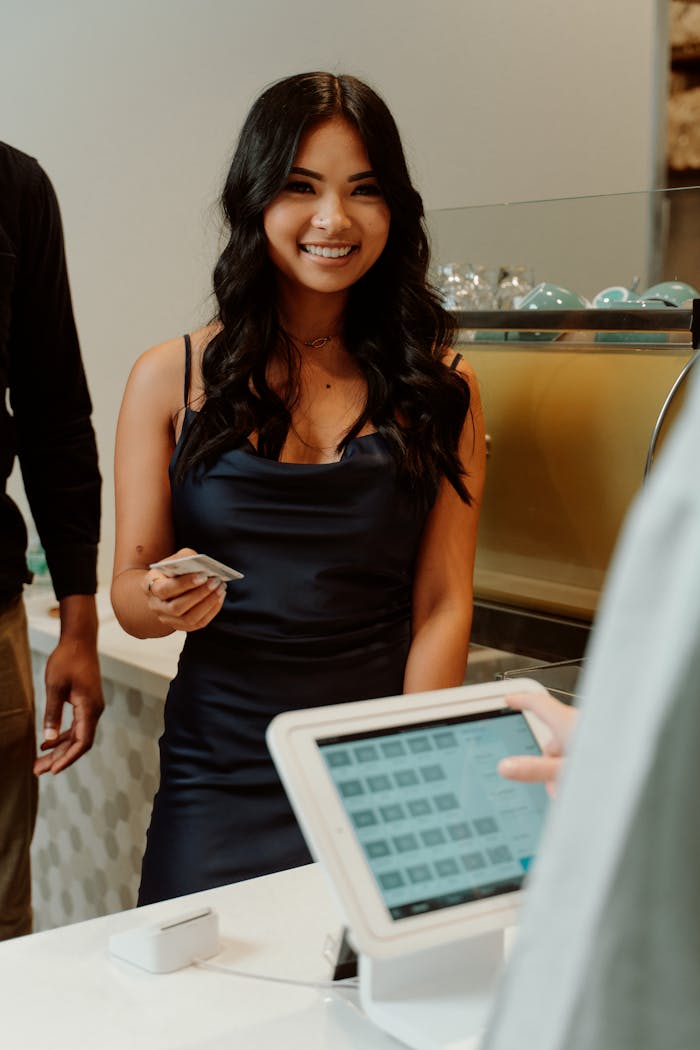 services-bg A woman in a black dress smiling while making a cashless payment at a store.