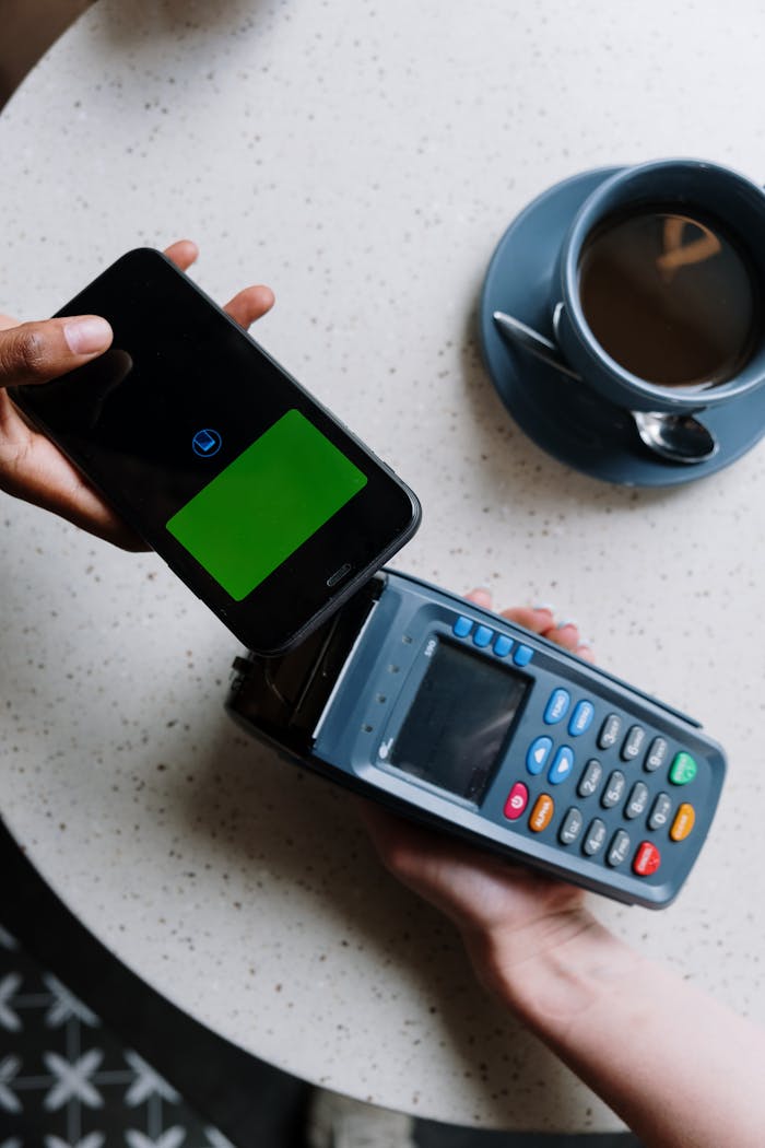 services-05 Smartphone making contactless payment on card reader next to coffee cup.