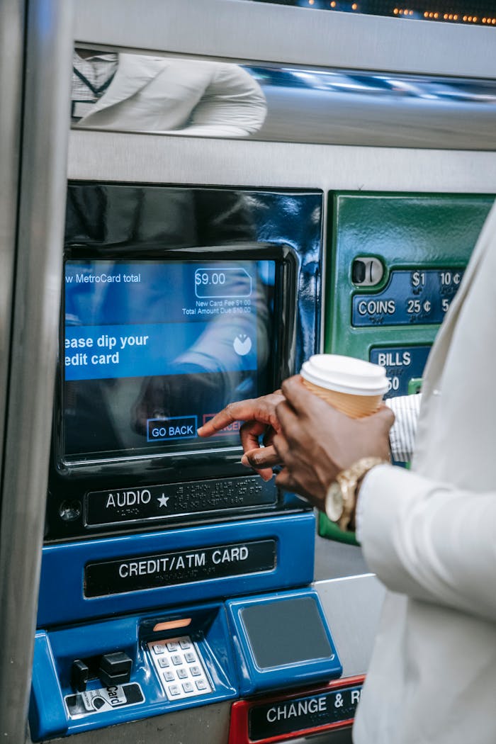 services-02 Close-up of a person using a subway ticket machine with a credit card and coffee cup.